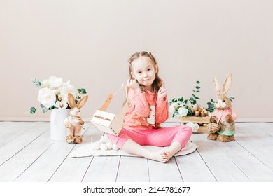 Little Girl Playing With Easter Toy Bunnies And A Basket Of Easter Eggs. Child Celebrating Easter. Easter Egg Hunt. Home Decoration, Bunnies And Flowers