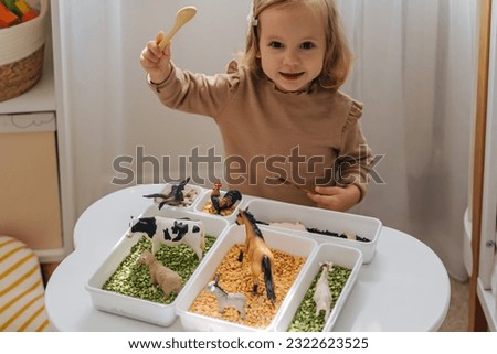 A little girl playing with farm animals in sensory bin in nursery. Educational game. Learning through play. Montessori material concept for toddlers. Sensory play ideas with small farm world play.