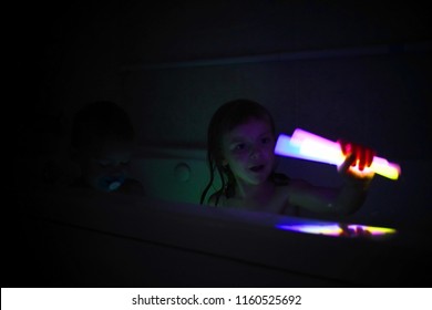 Little Girl Playing With Glow Sticks In The Bathtub With Her Little Brother