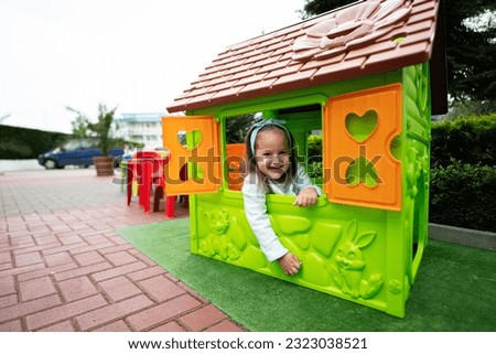 Little girl playing in green plastic kid house at children's playground. Child having fun outdoors.