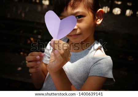 Little girl is playing with the heart shape paper that she cut it.