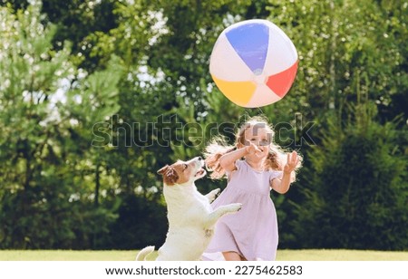 Little girl playing with her pet dog and beach ball at backyard lawn on summer day