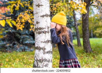 Little girl playing hide and seek in autumn forest outdoors
