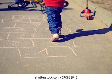 little girl playing hopscotch on asphalt outside
