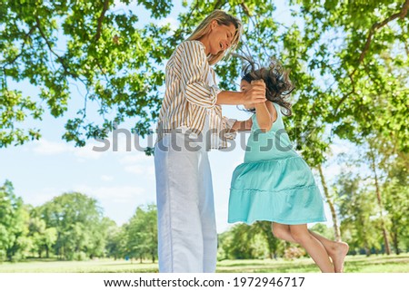 Little girl playing and jumping with her mother in the park on the grass during the picnic. Loving woman and daughter spending family time together on a sunny day. Mom and the kid have fun. 