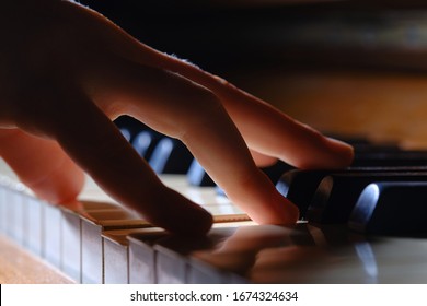 Little girl playing the old piano. Selective focus. Silhouette of children's fingers on the piano keyboard. Close up of young girls hand.