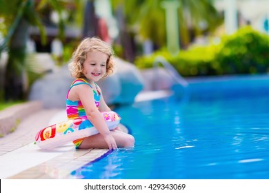 Little Girl Playing In Outdoor Swimming Pool In Tropical Resort. Child Learning To Swim. Toddler Kid With Inflatable Toy Ring. Summer Beach Vacation For Family With Children. Water Fun For Kids.