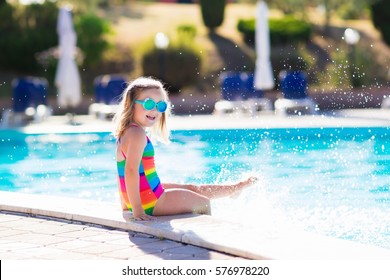 Little Girl Playing In Outdoor Swimming Pool Jumping Into Water On Summer Vacation On Tropical Beach Island. Child Learning To Swim In Outdoor Pool Of Luxury Resort. Water Toy And Sunglasses For Kids