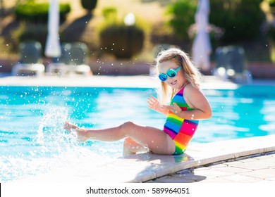 Little girl playing in outdoor swimming pool jumping into water on summer vacation on tropical beach island. Child learning to swim in outdoor pool of luxury resort. Water toy and sunglasses for kids.