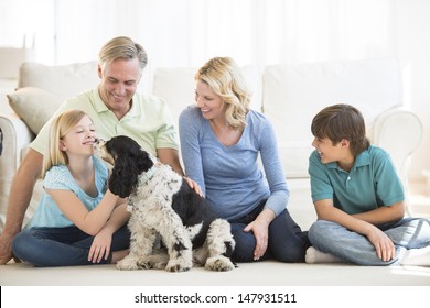 Little Girl Playing With Pet Dog While Family Looking At Her In Living Room