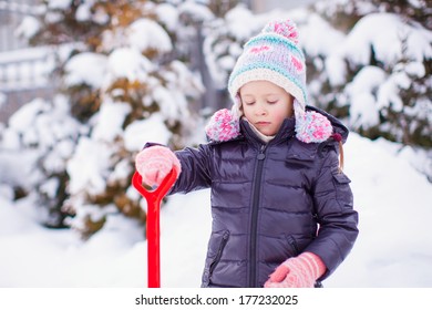 Little Girl Playing With Red Shovel In The Garden On Winter Day