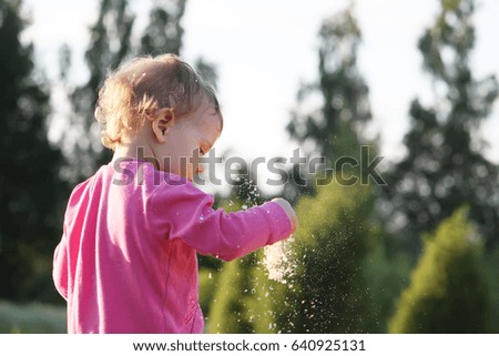 A little girl playing with sawdust outdoors on summer nature background.