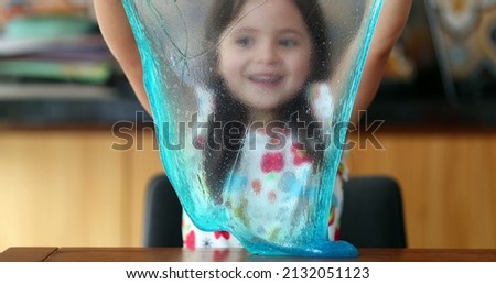 Little girl playing with slimy plasticine creating a bubble with blue slime