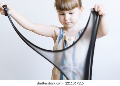 A Little Girl Is Playing With Slippery Slime. A Curious Little Girl Holds In Her Hands And Stretches The Black Slime. A Child Is Playing With A Slippery, Sticky Popular Toy. Entertainment For Children