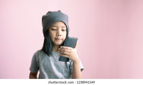 A Little Girl Playing Smartphone Selfie With Happiness And Smiling. Asian Girl Holding Phone With Gray Cloth Cap On The Pink Background With Copy Space.