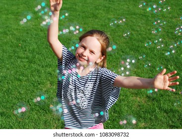 Little girl playing with soap bubbles. Cute smiling girl catching soap bubbles in the park on sunny day. Happy childhood.