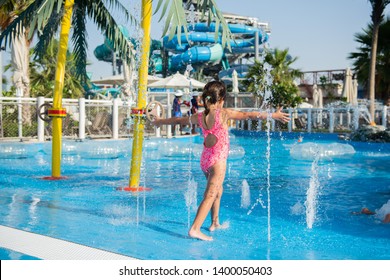 Little Girl Playing In A Swimming Pool With Fountains In A Water Park