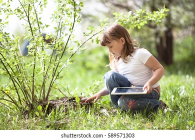Little girl playing with a tablet on a stump. Spring, childhood outdoors, exploring nature - Powered by Shutterstock