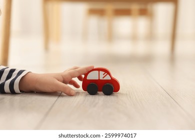 Little girl playing with toy car on floor at home, closeup. Space for text