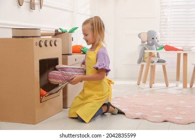 Little girl playing with toy cardboard oven at home - Powered by Shutterstock