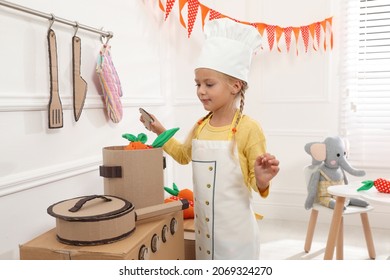 Little girl playing with toy cardboard kitchen at home
