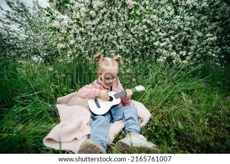 little girl playing the ukulele in a blooming apple orchard in nature