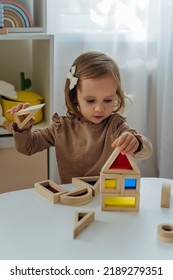 A Little Girl Playing With Wooden Blocks On The Table In Playroom.  Educational Game For Baby And Toddler In Modern Nursery. The Kid Builds A Tower From Wooden Rainbow Stacking Blocks.