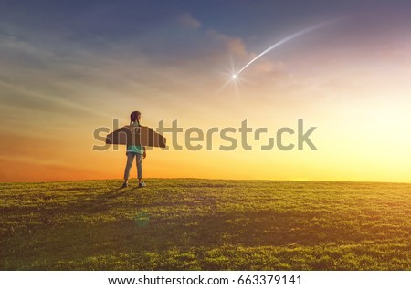 Little girl plays astronaut. Child on the background of sunset sky. Kid is looking at falling star and dreaming of becoming a spaceman.