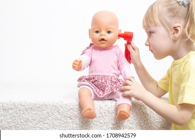 A little girl plays with a doll examines her ears. The concept of pediatric otolaryngology in medicine, treatment of otitis media and sulfur caps in children, copy space, damage