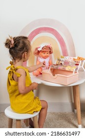 A Little Girl Plays With Doll And Hair Accessories In Children's Room. Girl Doing Hair To A Doll With Bows. Educational Game For Baby And Toddler In Modern Nursery. 