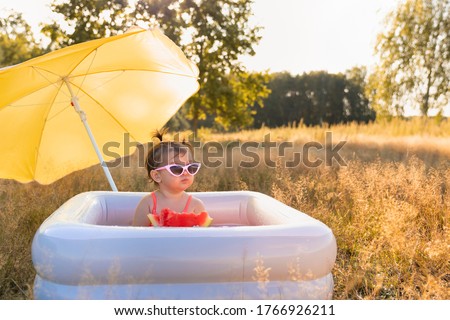 Little girl plays in the inflatable pool. The child eats a sweet watermelon, enjoy the summer and warmth. Carefree childhood.