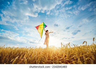 Little girl plays with a kite among ripe golden wheat field. Investing in the future, agriculture development concept. Ukraine Independence Day celebration.