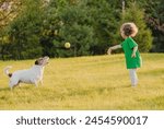 Little girl plays with pet dog on backyard lawn throwing toy ball to catch