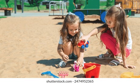 A little girl plays in the sandbox. Friendly sisters play together in the fresh air. Family summer holiday concept - Powered by Shutterstock