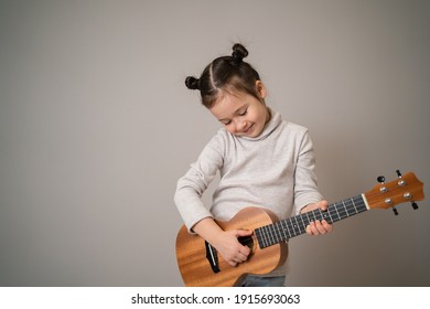 Little Girl Plays Ukulele. Creative Development In Children. Musical Education From Childhood. Teaching Music Online At Home