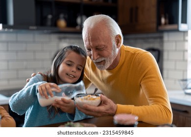 Little girl pouring milk into cornflakes cereals with grandpas help. Granddaughter and grandfather preparing morning meal together. Cheerful family moments, bonding and quality time. - Powered by Shutterstock