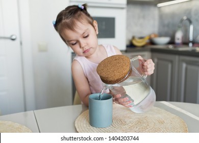 A little girl is pouring still water into a glass.  Morning breakfast. Kitchen table. - Powered by Shutterstock