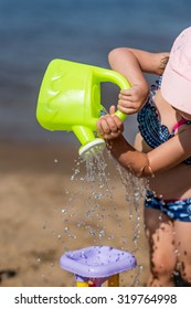 Little Girl Pours Water On The Water Mill On The Beach, Summer