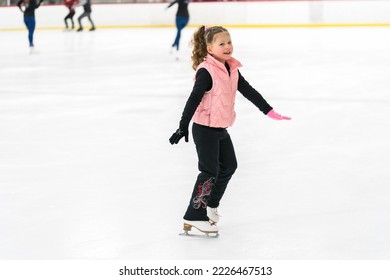 Niña pequeña practicando patinaje artístico en pista de patinaje sobre hielo interior.