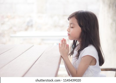 Little Girl Praying In The Morning On The Wooden Table.Little Asian Girl Hand Praying, Kid Praying To God,Hands Folded In Prayer Concept For Christianity, Faith, Spirituality And Religion.