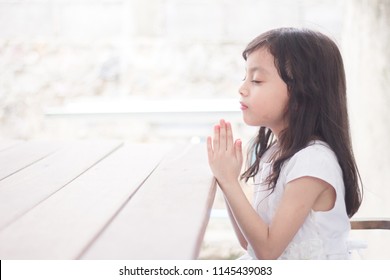 Little girl praying in the morning on the wooden table.Little asian girl hand praying, Kid praying to God,Hands folded in prayer concept for Christianity, faith, spirituality and religion.