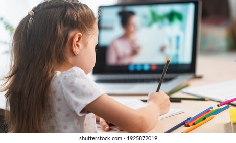 little girl, a preschooler, uses a laptop to study at home. the child smiles happily and receives knowledge remotely. digital concept of e-learning. Distance e-learning. View from over the shoulder