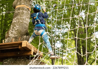 Little girl preschooler wearing full climbing harness having fun time in the rope park using carabiner and other safety equipment. Summer camp activity for kids. Adventure park in the forest - Powered by Shutterstock