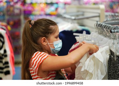 Little Girl In A Protective Medical Mask Chooses School Uniform Store.  Preparing For School. Prevention Of Coronavirus. Back To School Shopping.                            