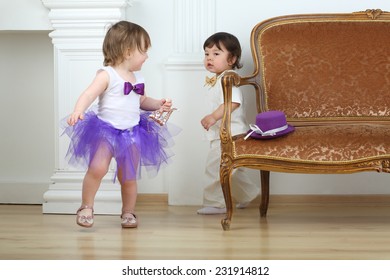 Little Girl In Purple Skirt Running Away From Boy In White Suit Around Sofa