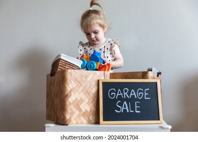 Little girl put her old toy on the box of things for a garage sale. Decluttering, cleaning and moderate consumption for a sustainable life