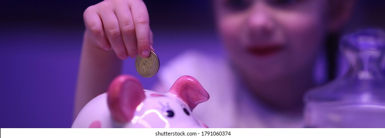 Little Girl Puts Coin In Piggy Bank On Table. Teach Child How To Save Money. Financial Literacy. Effectively Manage Any Cash Flows. Child Is Aware Philosophy Money And Learns Rules Dealing With Money