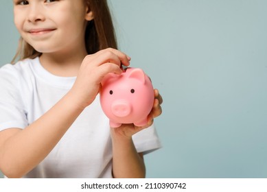 A Little Girl Puts A Coin In A Piggy Bank. The Concept Of Teaching Children Personal Finance And Saving.