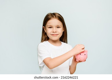 A Little Girl Puts A Coin In A Piggy Bank. The Concept Of Teaching Children Personal Finance And Saving.