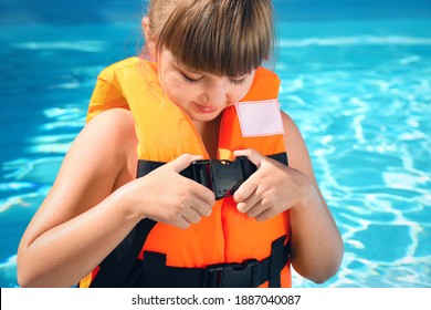 Little Girl Putting On Orange Life Vest In Swimming Pool